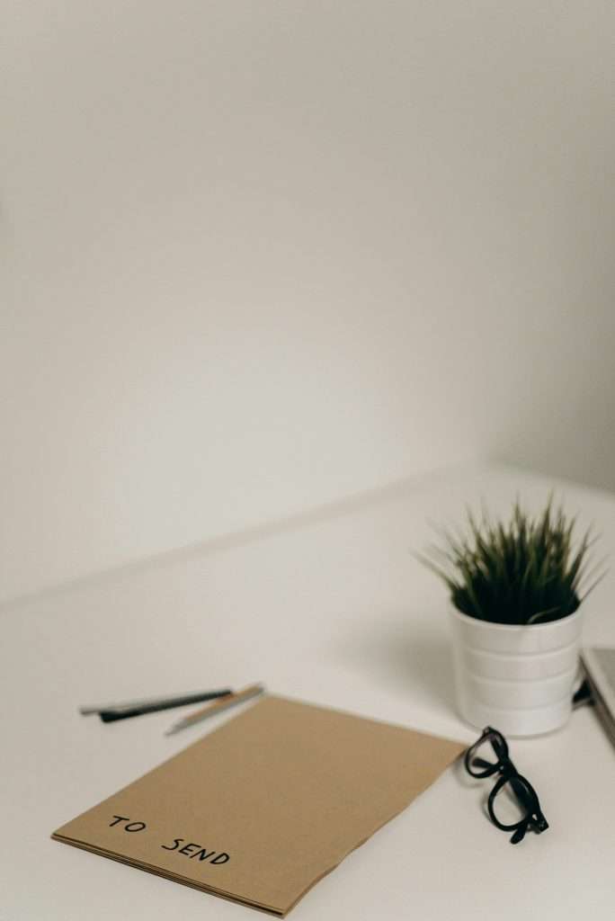 A clean, minimalist desk setup with envelope labeled 'To Send', glasses, and plant.